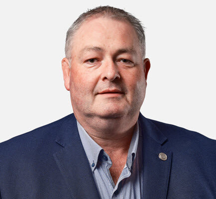 Middle-aged man with short gray hair wearing a blue blazer and light blue shirt, looking directly at the camera against a plain white background.